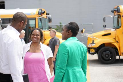 People speak in a parking lot near school buses.