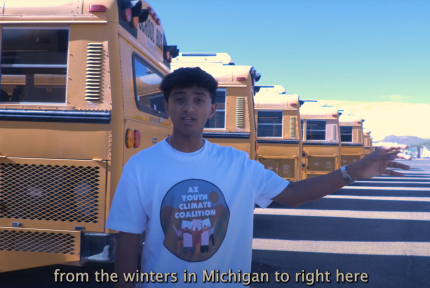 Boy stands in front of row of school buses.