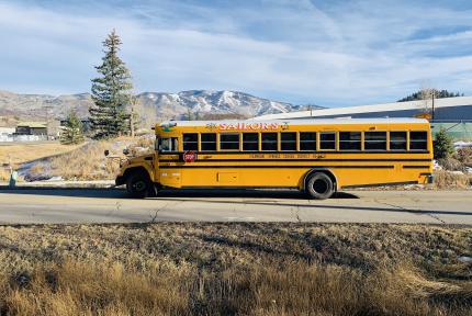 A yellow electric school bus outside on the road in front of mountains.