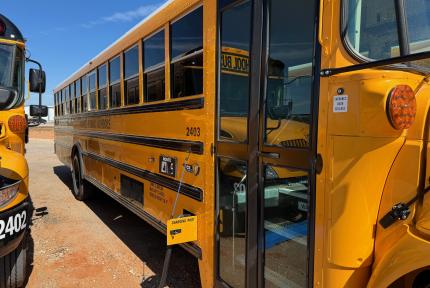 An electric school bus charges while parked under the sun