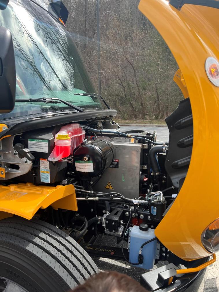 The open front hood of an electric school bus, showing the electric battery and related systems.