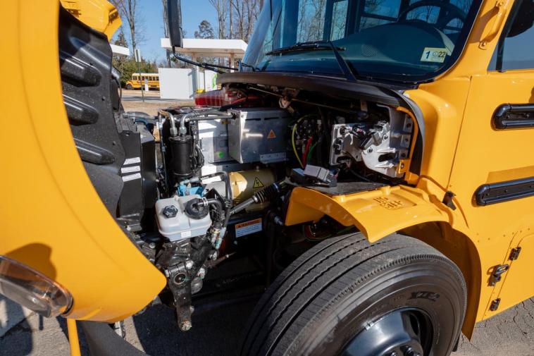 The front hood of an electric school bus is open, revealing the battery-powered engined and the accompanying system.