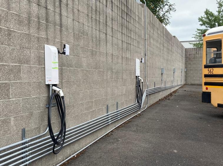 Electric school bus chargers and access points mounted to a brick wall, near the back of an electric school bus.