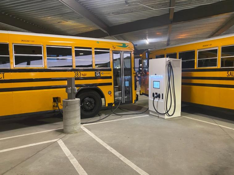 Two electric school buses at a charging station.