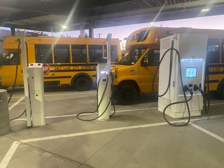 Two electric school buses at charging stations.