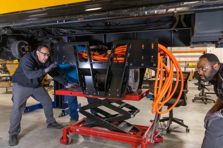 As part of the repower process, technicians install an electric motor and high-voltage cables between the school bus chassis frame rails