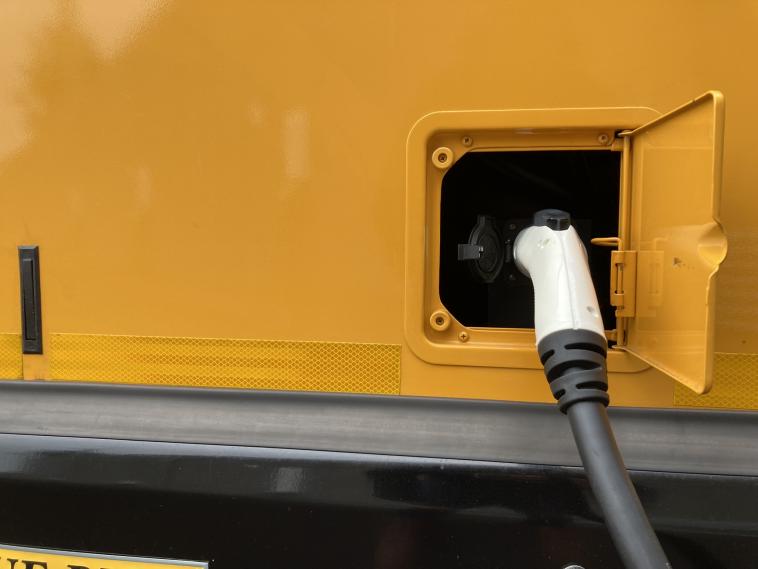 An electric school bus charger plugged into a port.