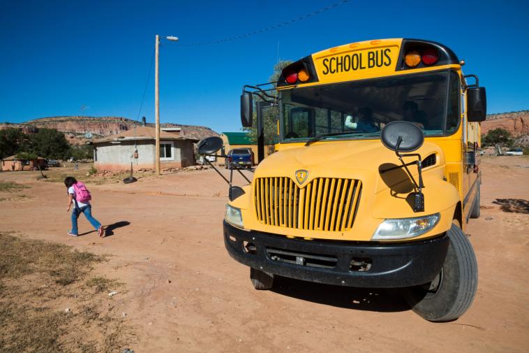 A student jogs away from a school bus on a dirt road.