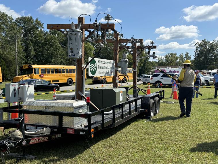 Electric equipment on a truck bed in a grass field, near school buses.  