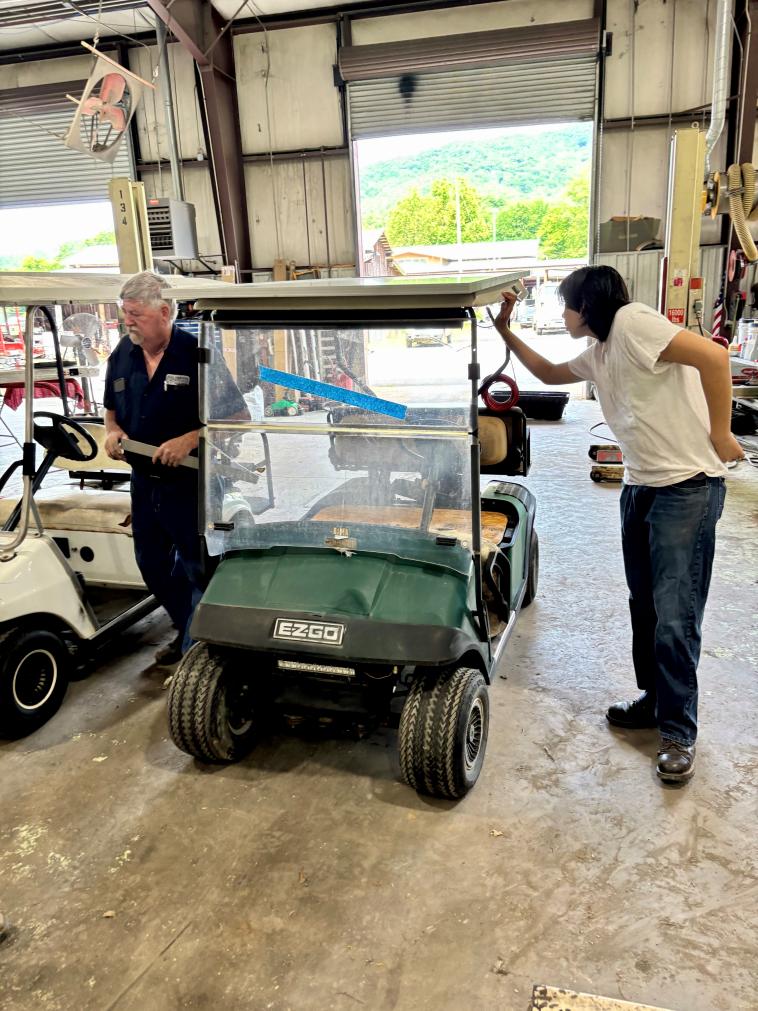 Two people stand near a golf cart in a garage.