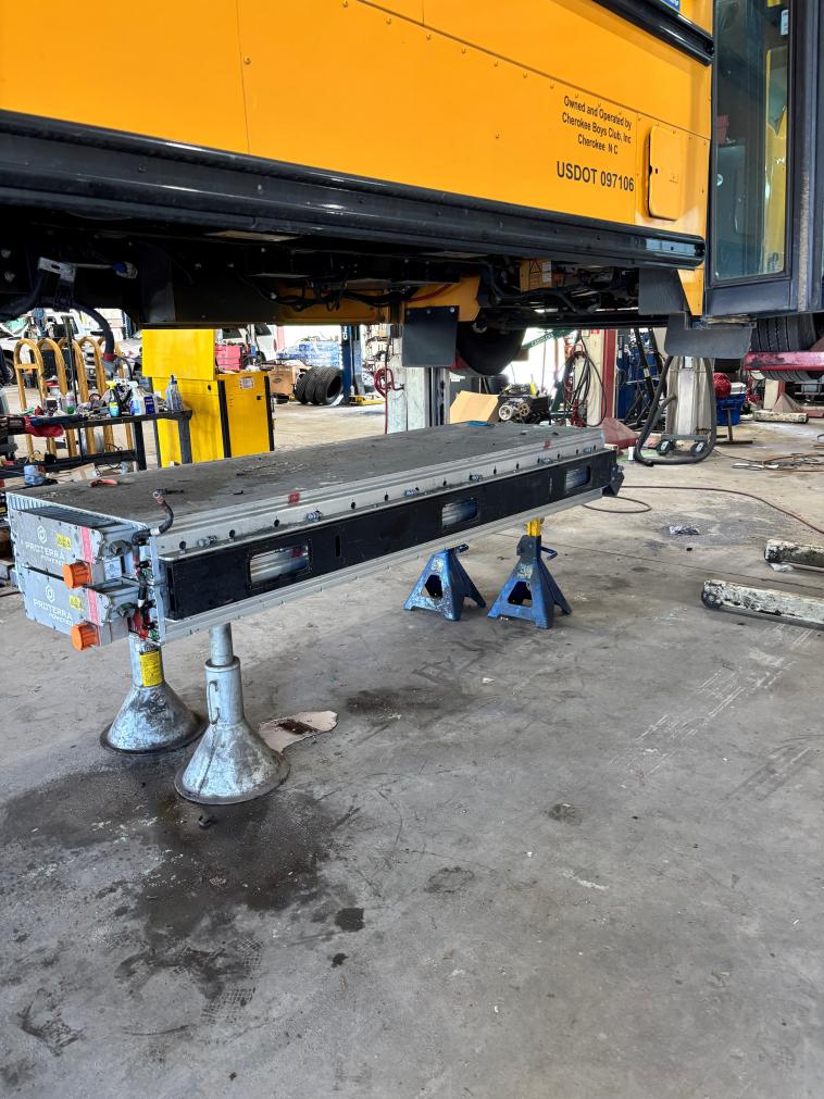 An electric school bus battery pack sits underneath an elevated electric school bus chassis