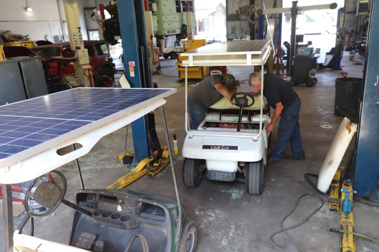 Two men work on a golf cart
