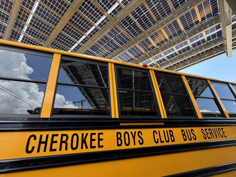Side of an electric school bus reads "Cherokee Boys Club Bus Service"