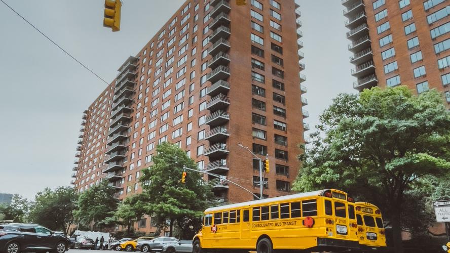 A school bus parked in a city next to a multi-story residential building.
