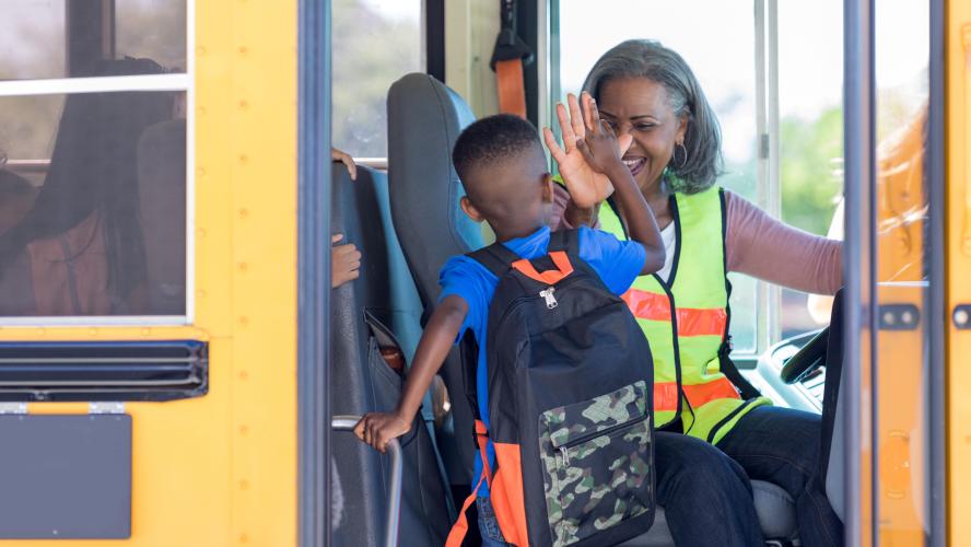 A bus driver high-fives a student boarding a school bus.
