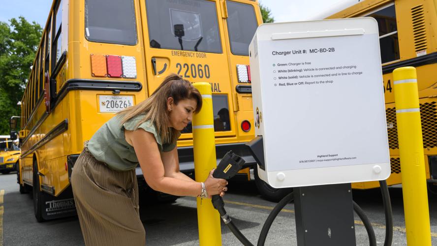 A worker plugs an electric school bus in to a charger.