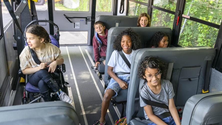 Diverse group of students, with and without disability, riding an accessible school bus.