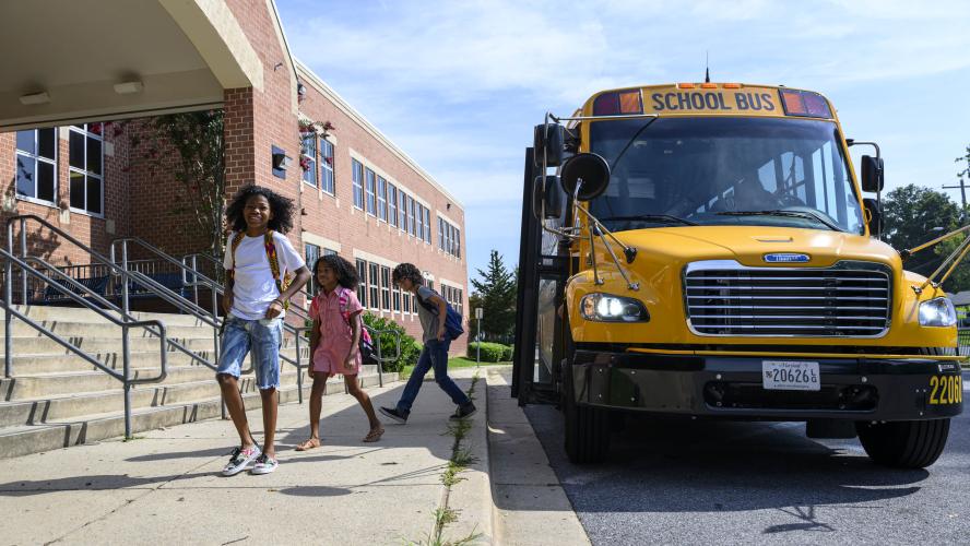 Three students step off an electric school bus in front of a school.