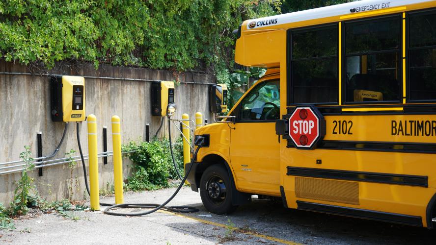 A yellow electric school bus is parked and plugged in to a charger.
